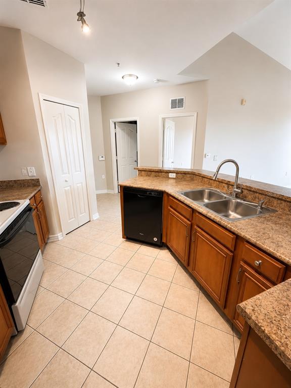A kitchen with wood cabinets, laminate countertops, a black dishwasher, and tile flooring — 6157 METROWEST BOULEVARD UNIT 308, ORLANDO, FL