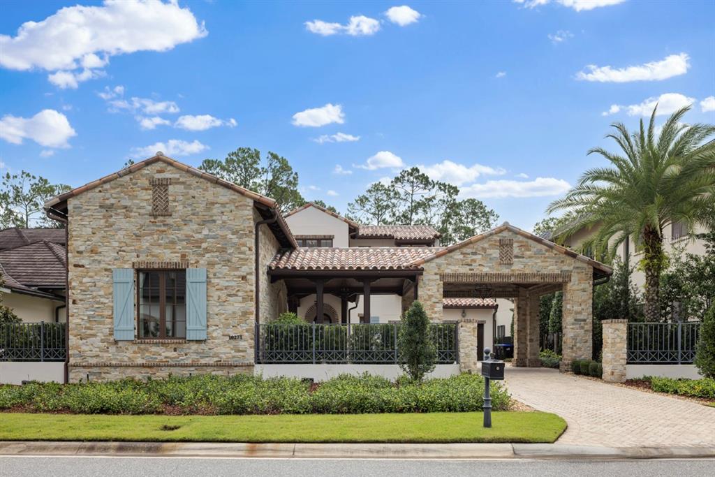 A stone-clad house features a tiled roof, light blue shutters, and a gated driveway entrance — 10271 SYMPHONY GROVE DRIVE, GOLDEN OAK, FL