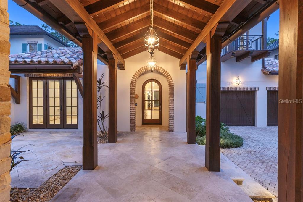 A covered stone walkway leads to an arched wooden door between two building wings — 10271 SYMPHONY GROVE DRIVE, GOLDEN OAK, FL