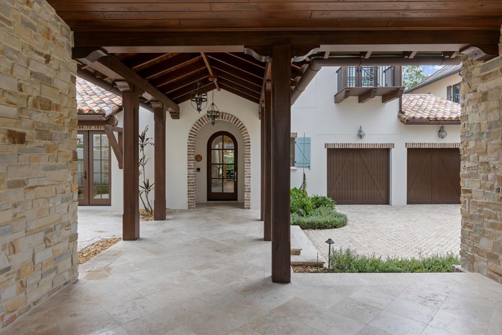 A covered stone patio leads to an arched wooden front door with a brick surround — 10271 SYMPHONY GROVE DRIVE, GOLDEN OAK, FL