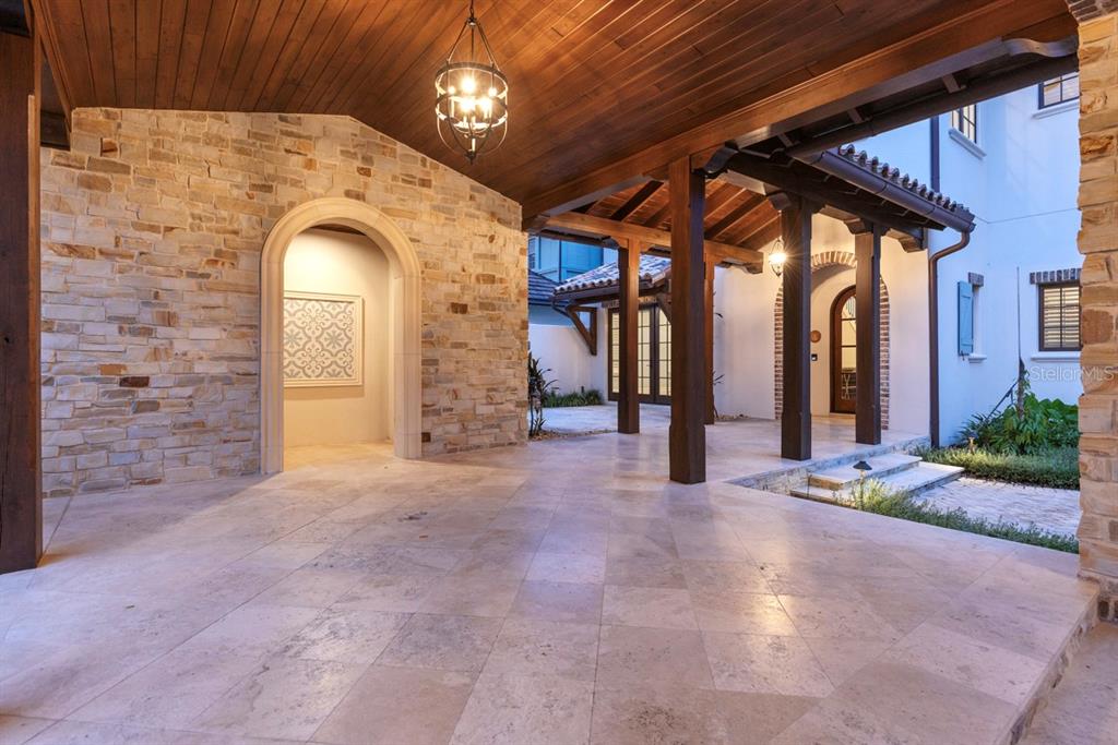 A covered stone patio features a wood-paneled ceiling, arched entryways, and large tile flooring — 10271 SYMPHONY GROVE DRIVE, GOLDEN OAK, FL