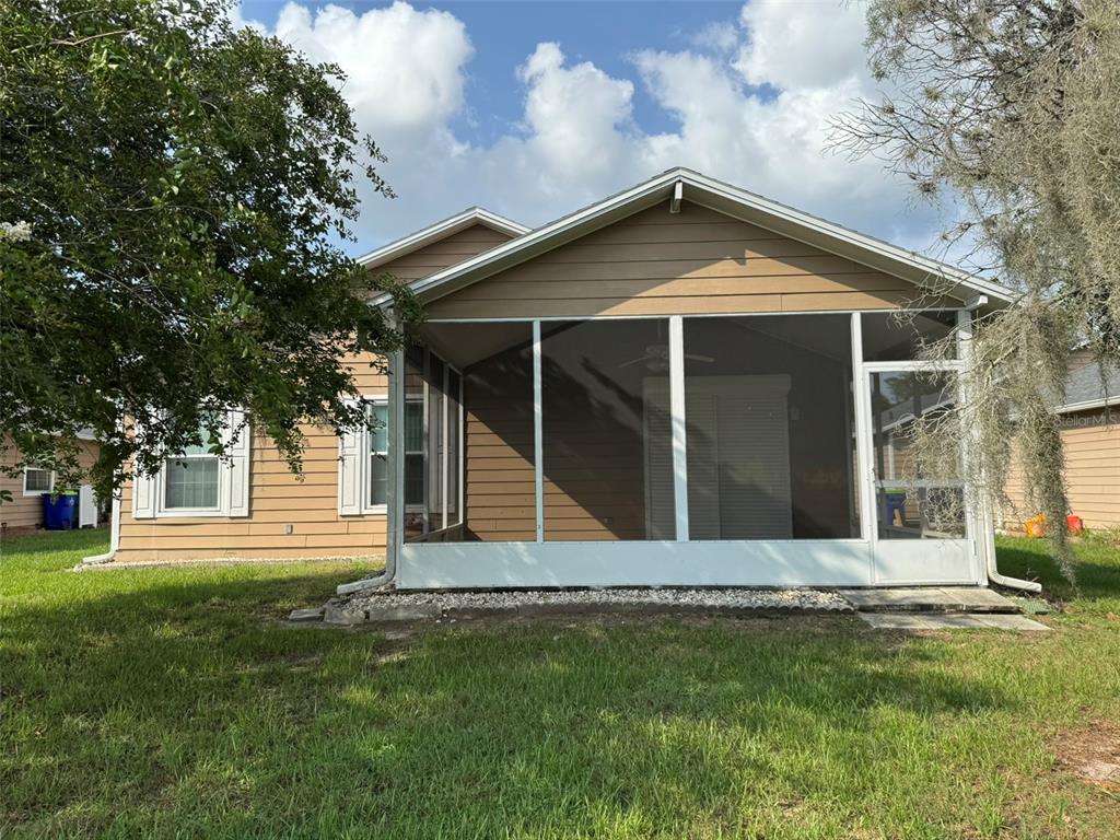 A tan house features a screened-in back porch with white framing and a grassy yard — 37414 CASTLEBERRY DRIVE, ZEPHYRHILLS, FL