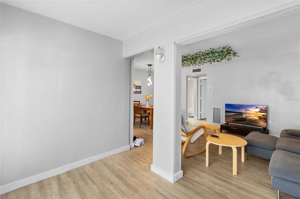 A living room with light wood-look flooring opens into a dining area and hallway — 1221 DREW STREET UNIT B3, CLEARWATER, FL
