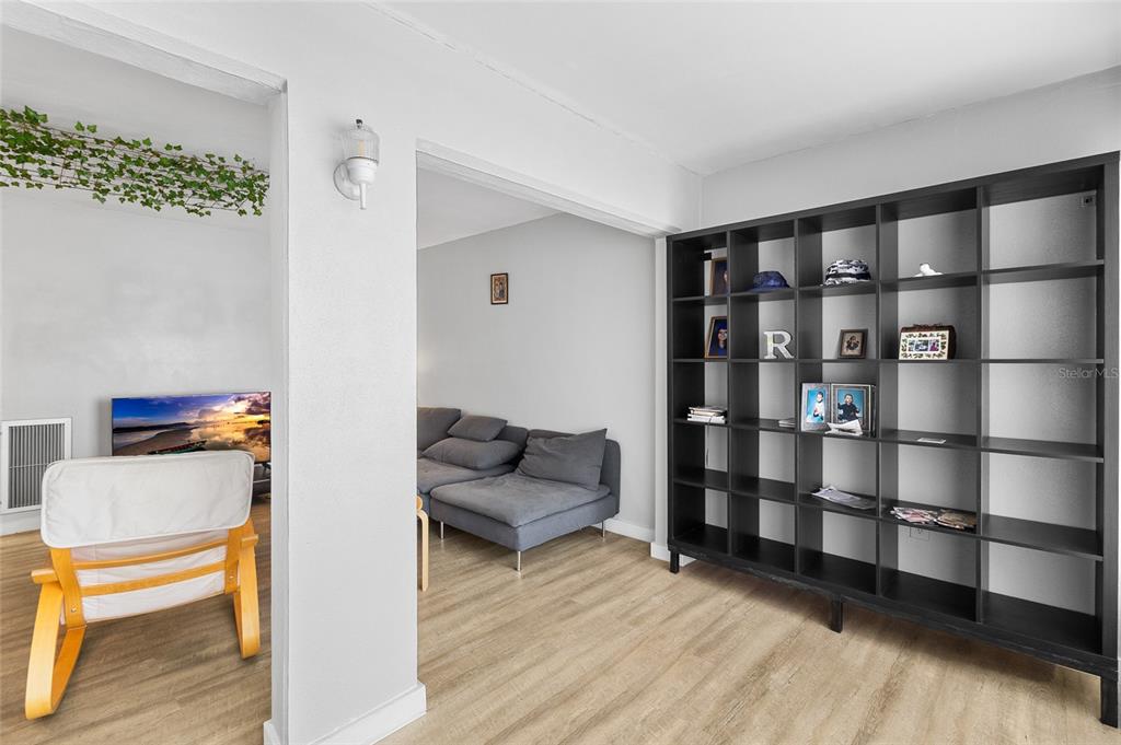 A living area features light wood flooring, a black shelving unit, and an adjacent seating space — 1221 DREW STREET UNIT B3, CLEARWATER, FL