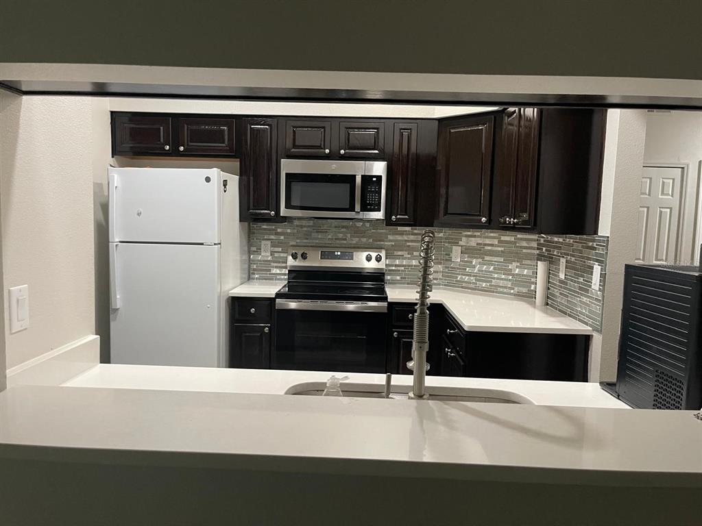 A kitchen features dark wood cabinets, white countertops, stainless steel appliances, and a tiled backsplash — 13303 PINYON DRIVE, CLERMONT, FL
