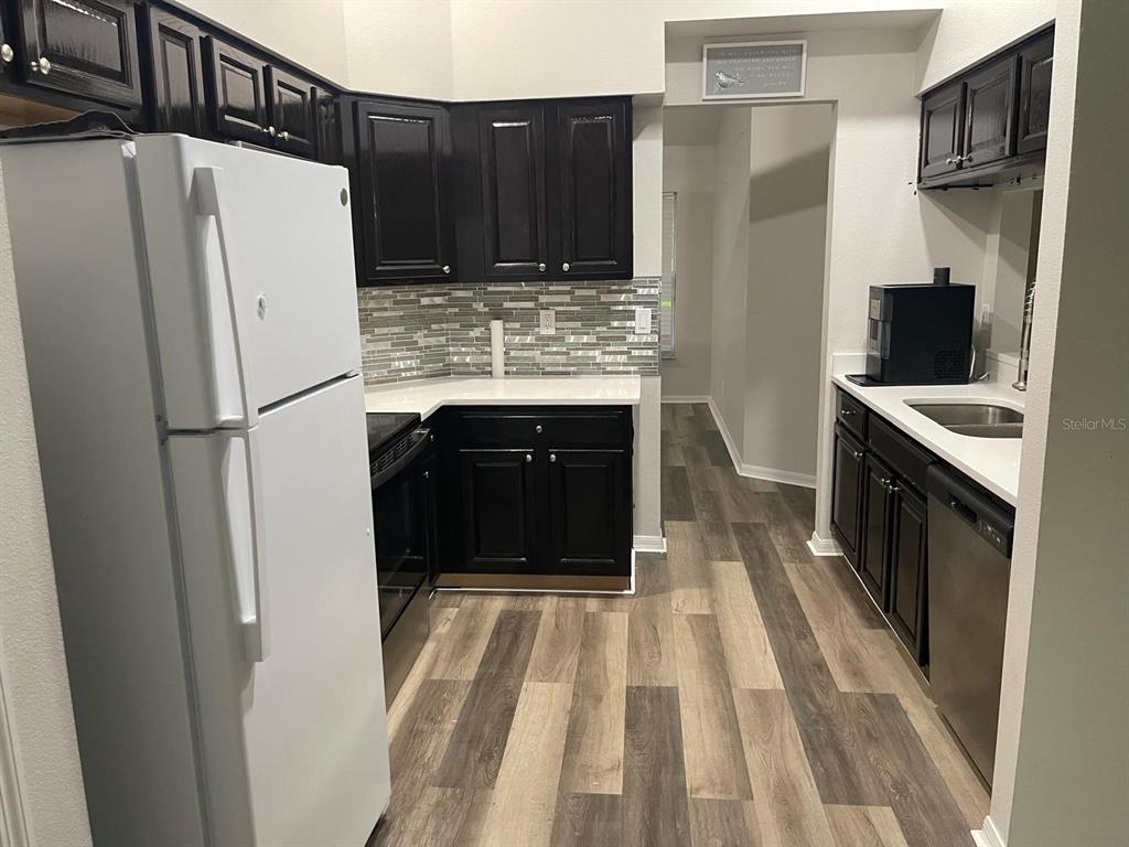 A kitchen features black cabinets, white countertops, a tiled backsplash, and wood-look flooring — 13303 PINYON DRIVE, CLERMONT, FL