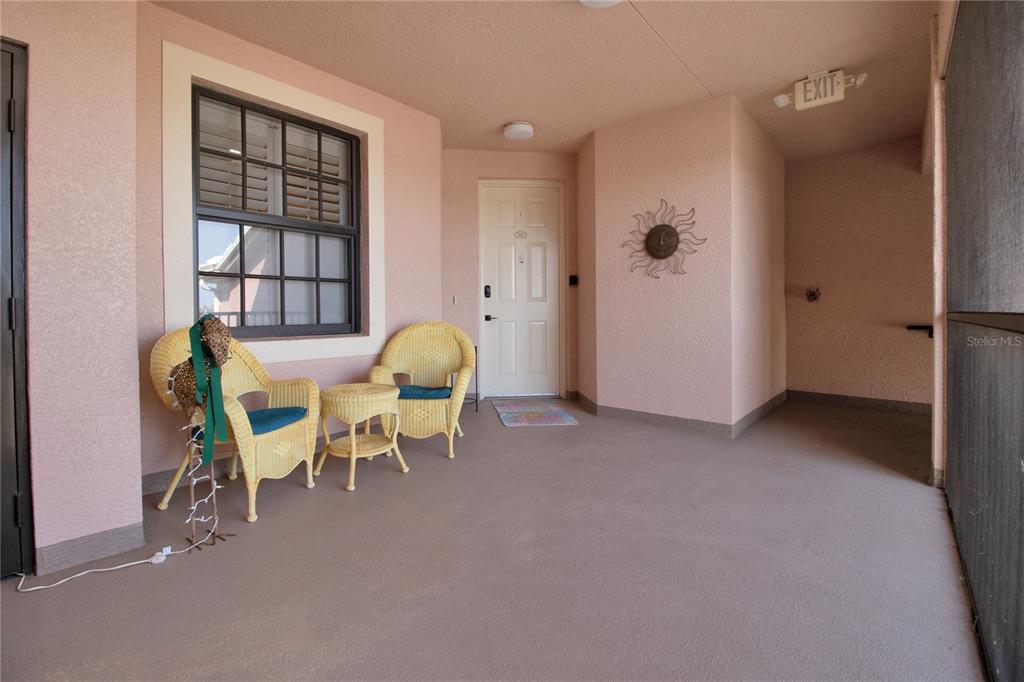 A covered balcony features two wicker chairs, a small table, and a light-colored door — 24417 BALTIC AVENUE UNIT 1302, PUNTA GORDA, FL
