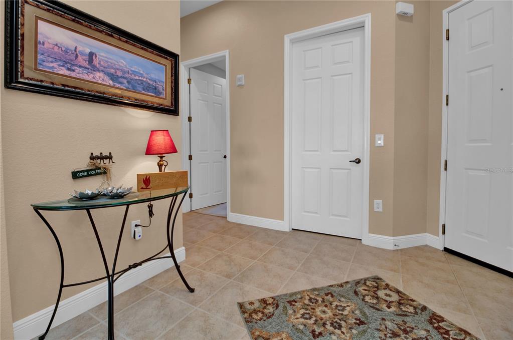 A tiled entryway features a glass-topped console table, a framed landscape painting, and two doors — 24417 BALTIC AVENUE UNIT 1302, PUNTA GORDA, FL