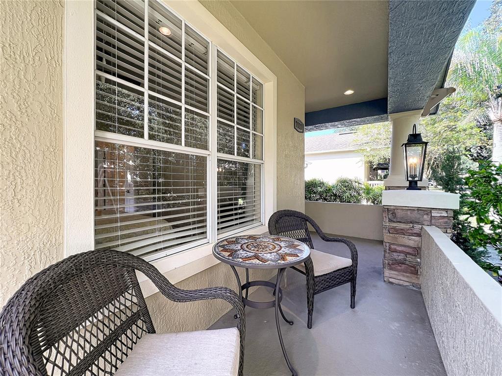 A covered front porch features two wicker chairs, a mosaic table, and a stone pillar — 7033 BRAMLEA LANE, WINDERMERE, FL