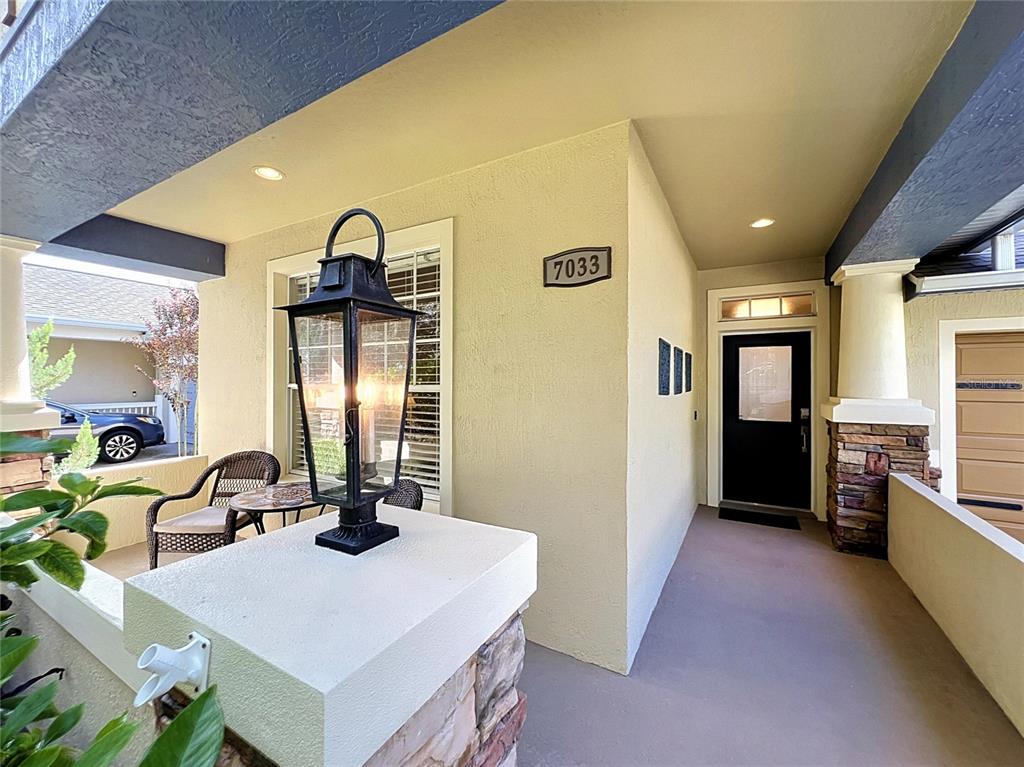 A covered entryway features a stone-accented pillar, a black lantern, and a dark front door — 7033 BRAMLEA LANE, WINDERMERE, FL