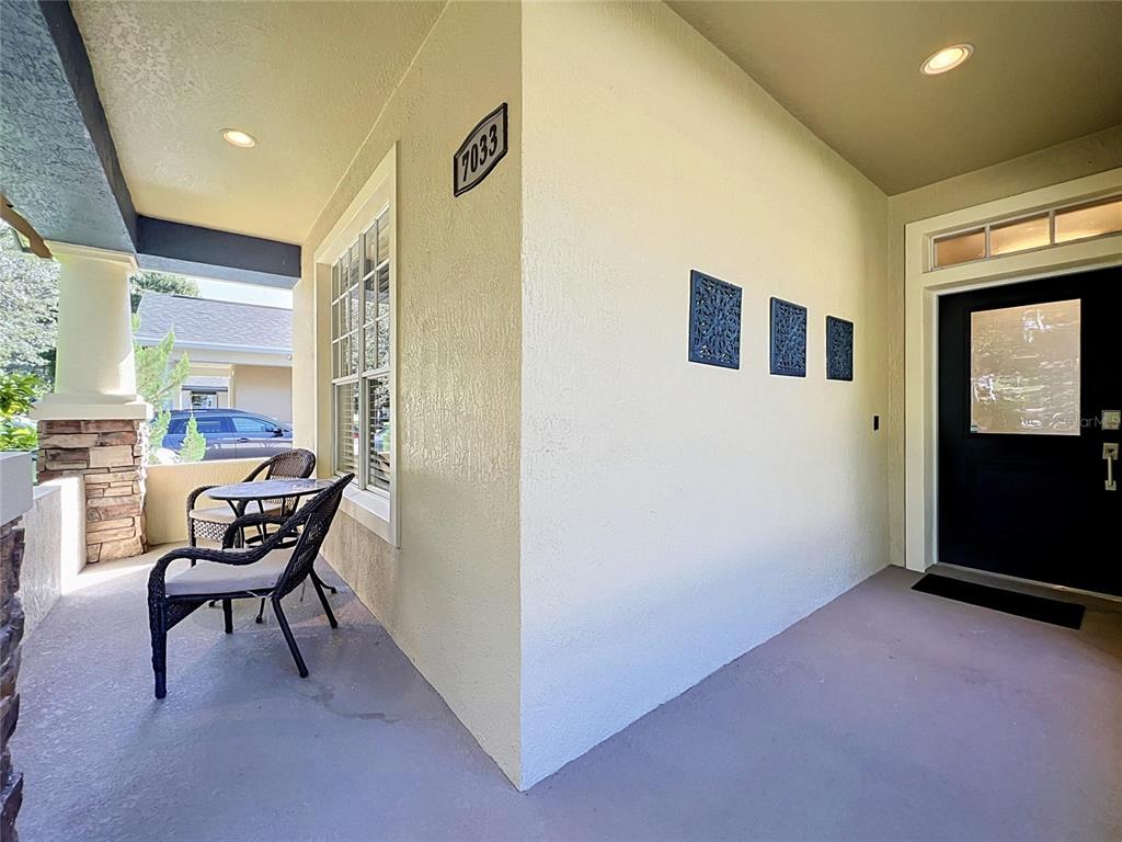 A covered front porch features a seating area, a black door, and decorative wall accents — 7033 BRAMLEA LANE, WINDERMERE, FL