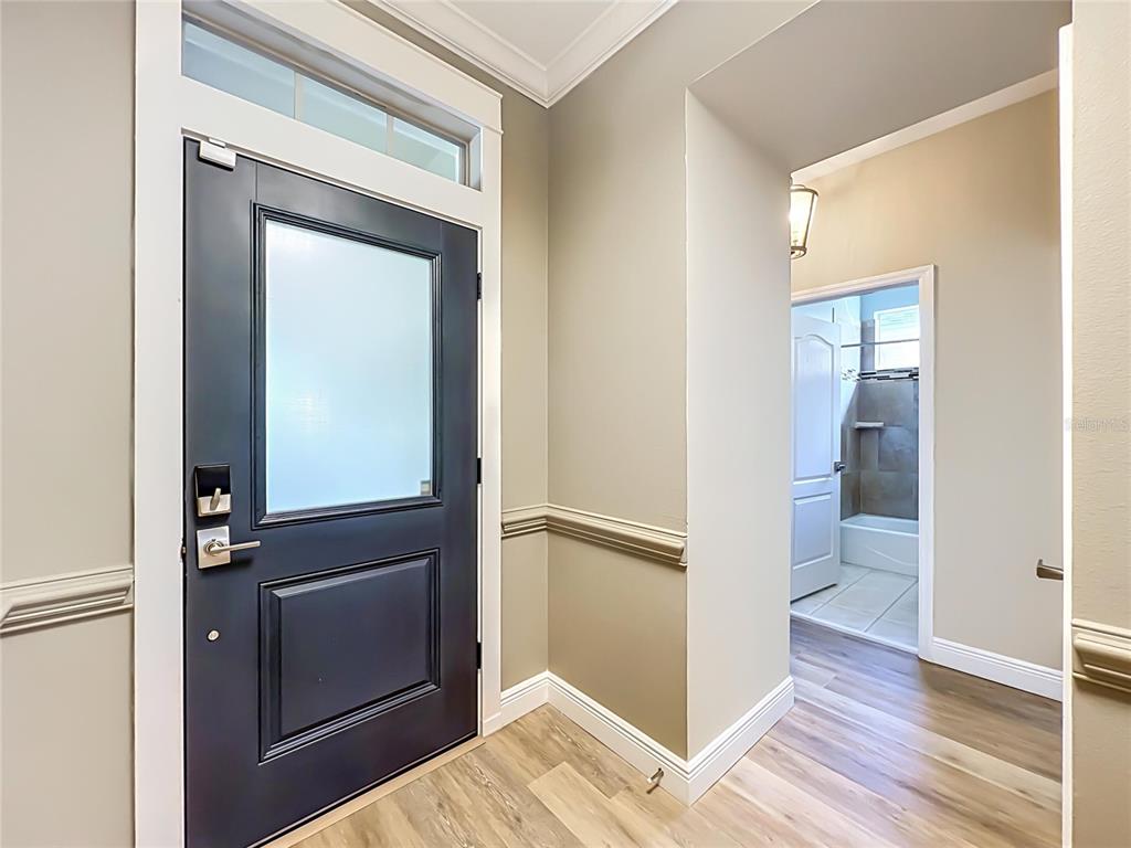 An entryway features a dark door with a frosted glass panel and light wood flooring — 7033 BRAMLEA LANE, WINDERMERE, FL