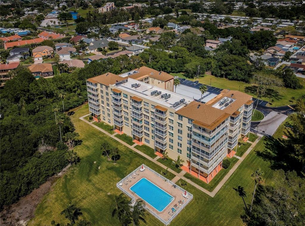 An aerial view of a multi-story apartment building with a swimming pool and surrounding landscaping — 9000 COMMODORE DRIVE UNIT 302, SEMINOLE, FL