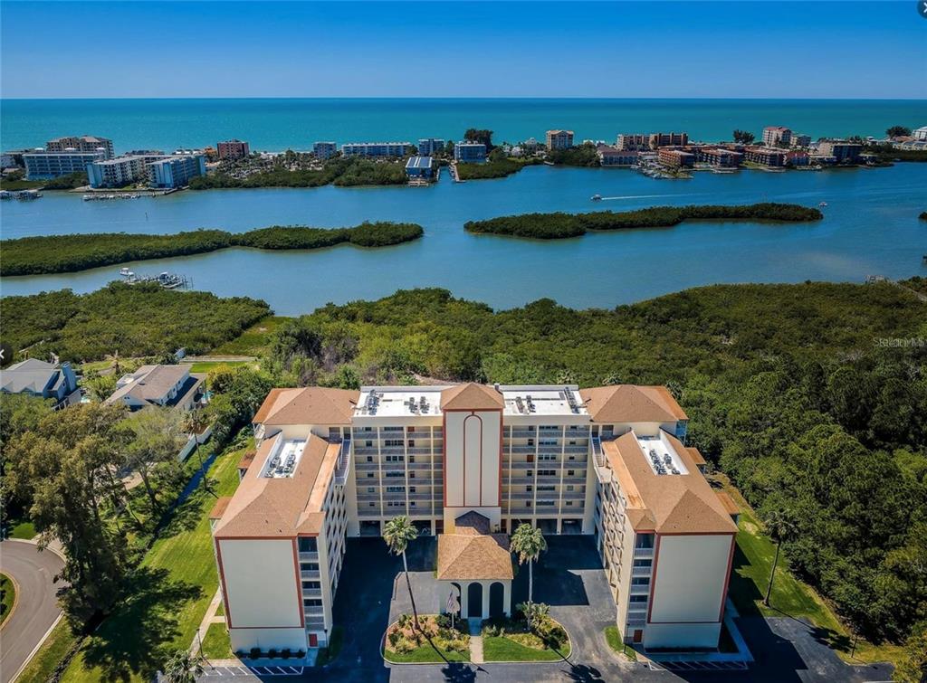An aerial view of a multi-story apartment building situated near a bay and the ocean — 9000 COMMODORE DRIVE UNIT 302, SEMINOLE, FL