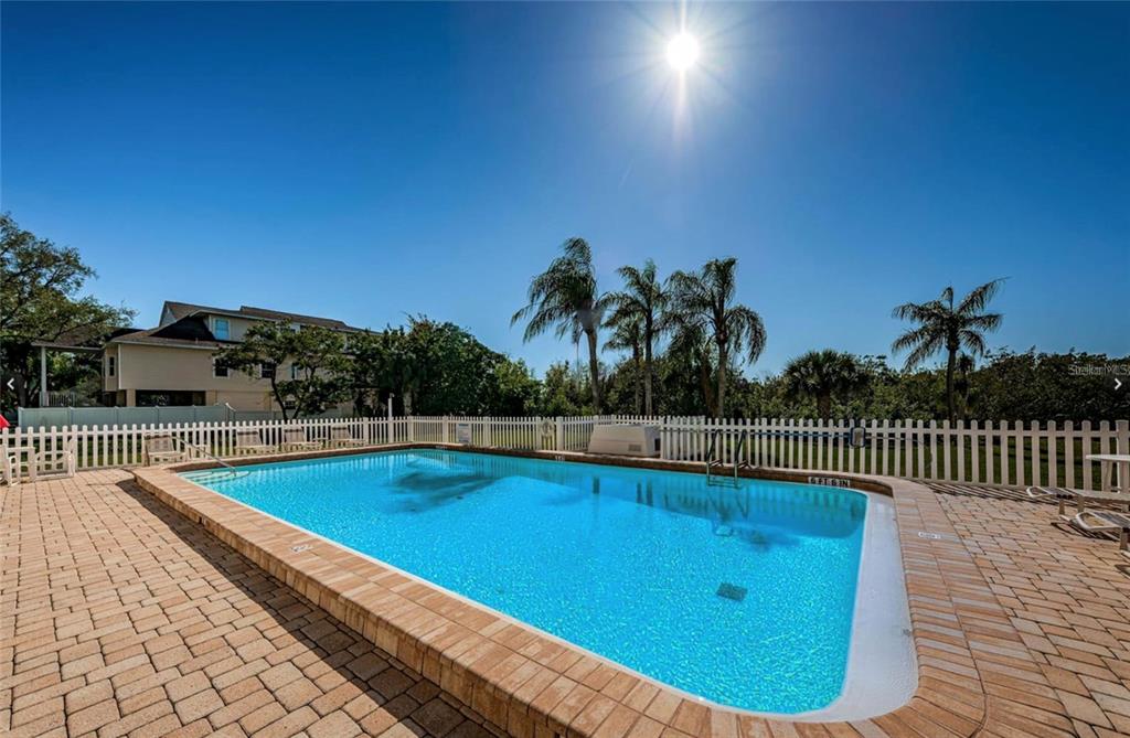 A rectangular swimming pool with a brick paver deck is enclosed by a white fence — 9000 COMMODORE DRIVE UNIT 302, SEMINOLE, FL