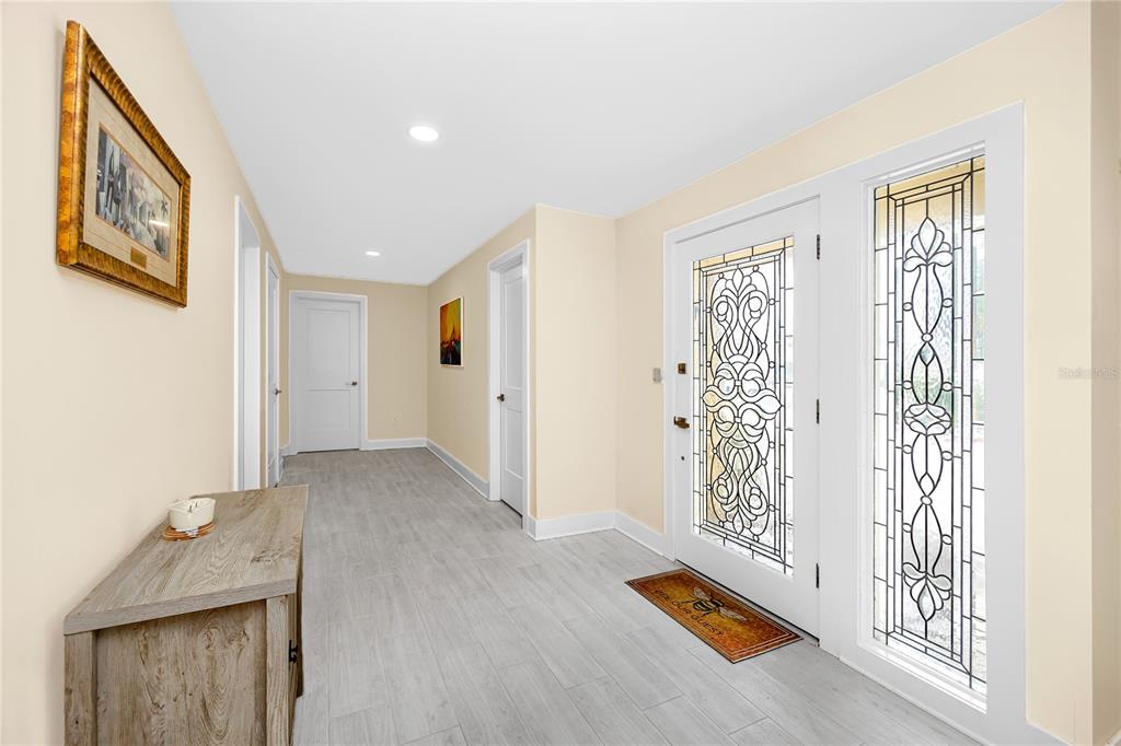 A bright entryway features light wood-look flooring, white doors, and a decorative glass front door — 107 21ST STREET, BELLEAIR BEACH, FL