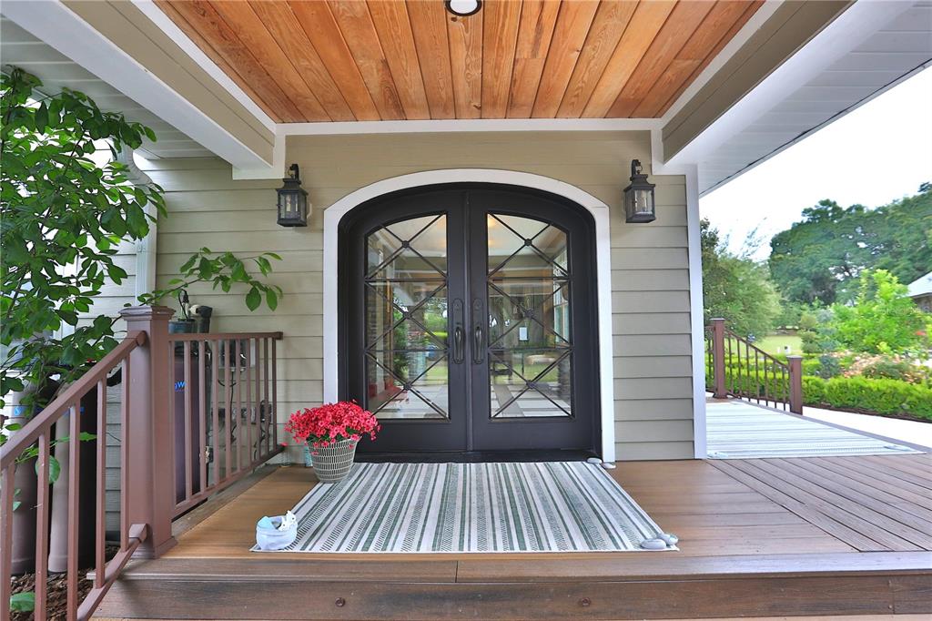 A covered wooden porch features a dark arched double door with glass panes and lanterns — 19650 NE 17TH PLACE, WILLISTON, FL