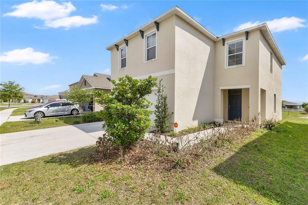 A two-story beige house with a concrete driveway, a front yard, and a dark door — 167 EAGLEVIEW LOOP, DAVENPORT, FL
