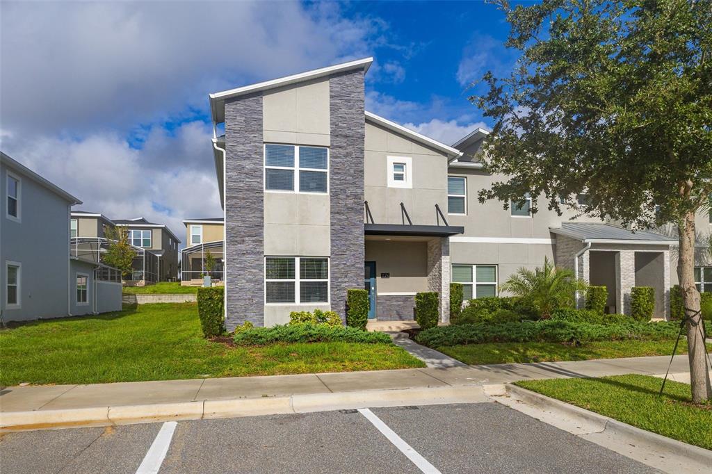 A two-story townhouse exterior features gray stucco, stone accents, and a modern front door — 1176 CHALLENGE DRIVE, DAVENPORT, FL