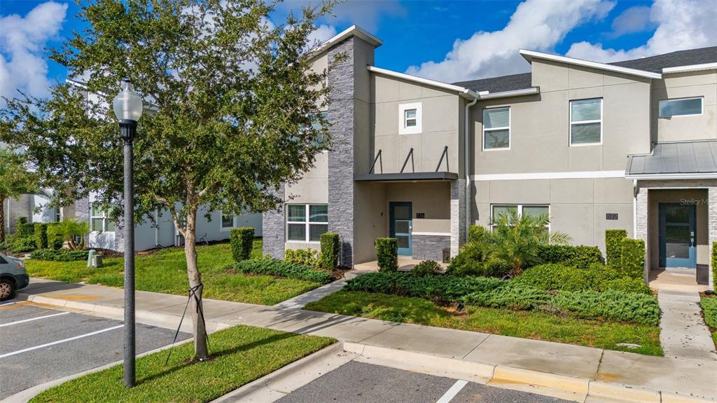 The exterior of a two-story home features gray stone accents, a dark blue door, and landscaping — 1176 CHALLENGE DRIVE, DAVENPORT, FL