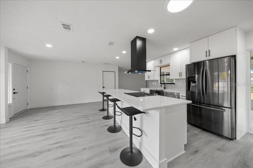 A modern kitchen features white cabinets, a central island with bar stools, and stainless appliances — 59 SILVER PLACE, OCALA, FL