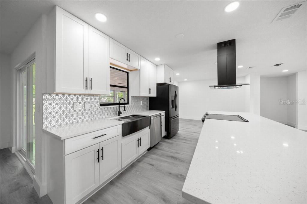 A modern kitchen features white cabinets, a large island, black appliances, and a geometric backsplash — 59 SILVER PLACE, OCALA, FL