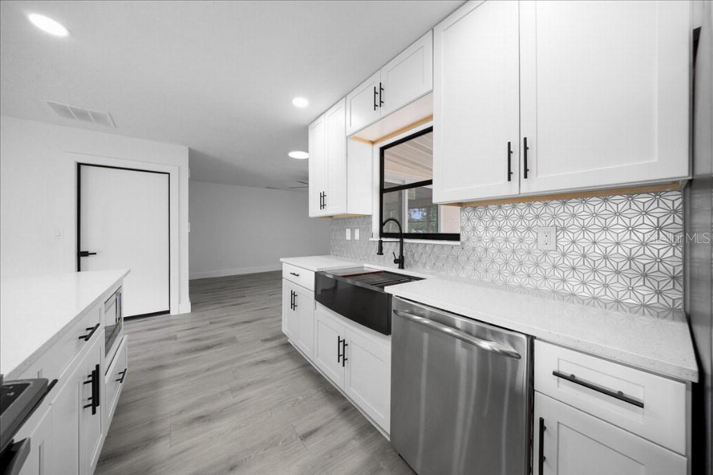 A modern kitchen features white cabinets, a black farmhouse sink, and a geometric tile backsplash — 59 SILVER PLACE, OCALA, FL