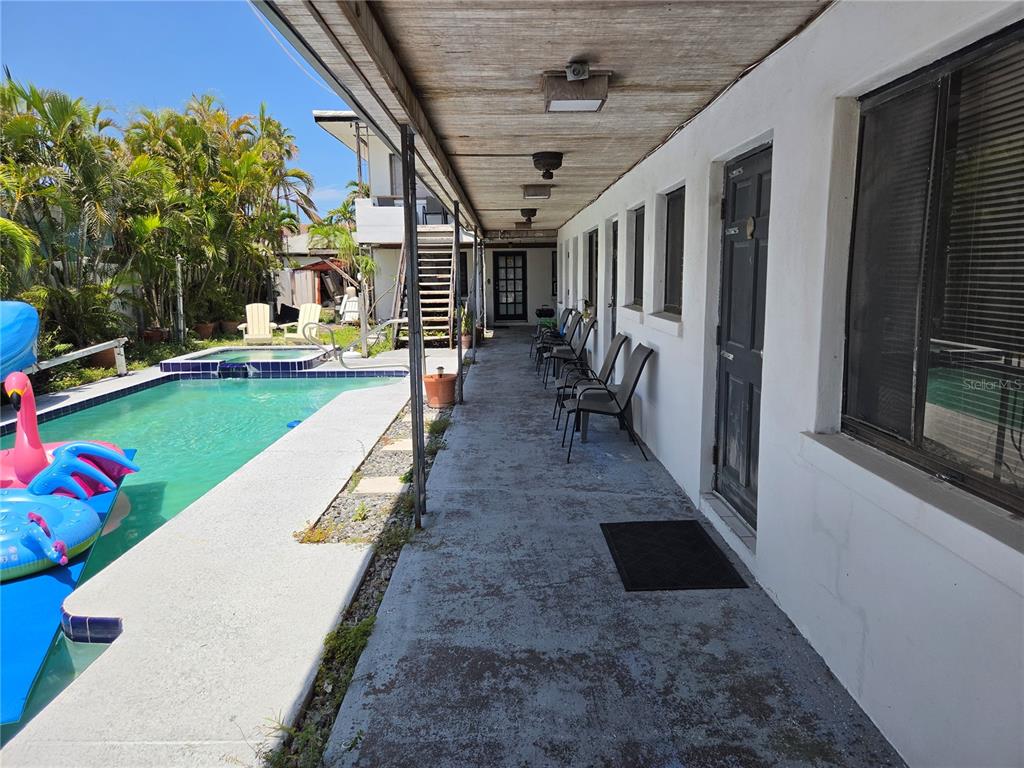 A concrete walkway runs alongside a swimming pool and a row of exterior building doors — 580 BAY ESPLANADE, CLEARWATER BEACH, FL