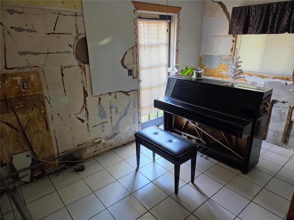 A room with white tile flooring, a black piano, and walls showing exposed construction materials — 580 BAY ESPLANADE, CLEARWATER BEACH, FL