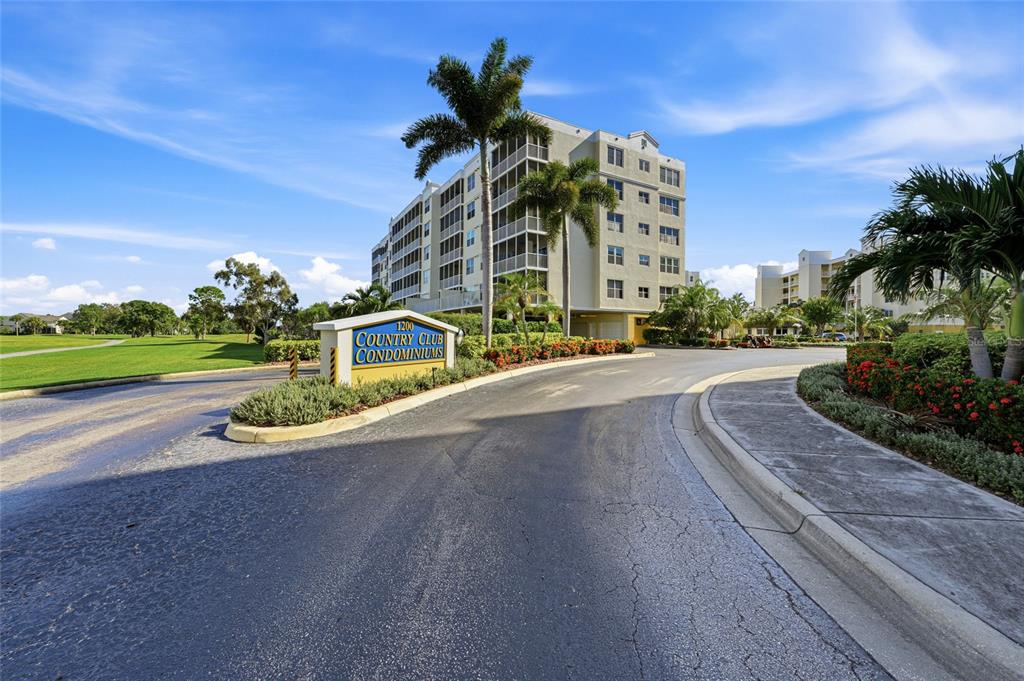 A multi-story condominium building stands behind a sign at the entrance of a paved driveway — 1200 COUNTRY CLUB DRIVE UNIT 4201, LARGO, FL