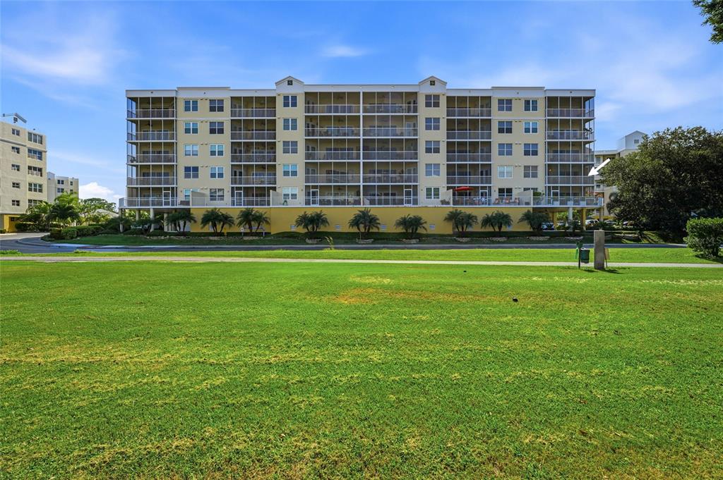 A multi-story apartment building with screened balconies sits behind a large, open grassy lawn — 1200 COUNTRY CLUB DRIVE UNIT 4201, LARGO, FL