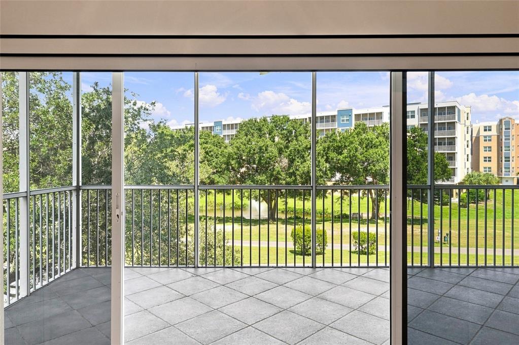 A screened-in balcony with tile flooring overlooks a grassy lawn, trees, and a pond — 1200 COUNTRY CLUB DRIVE UNIT 4201, LARGO, FL