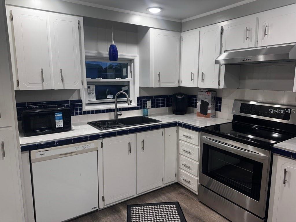 A kitchen features white cabinets, dark blue tiled backsplashes, and stainless steel appliances — 530 SUN UP STREET, NORTH FORT MYERS, FL