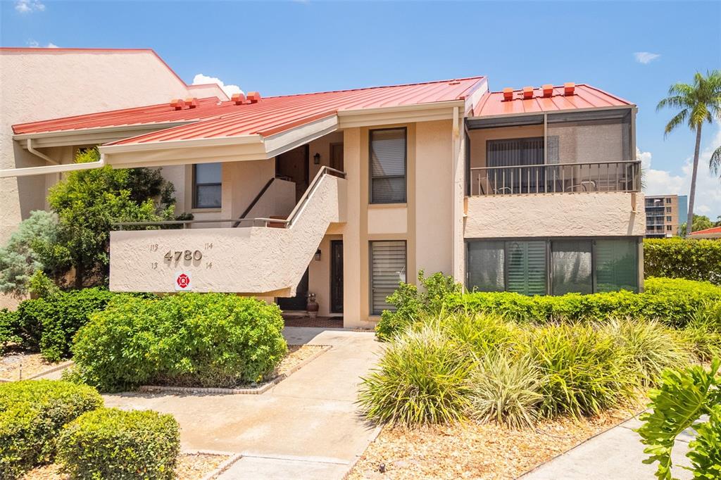A two-story tan stucco building features a red metal roof and an exterior staircase — 4780 BRITTANY DRIVE S UNIT 114, ST PETERSBURG, FL