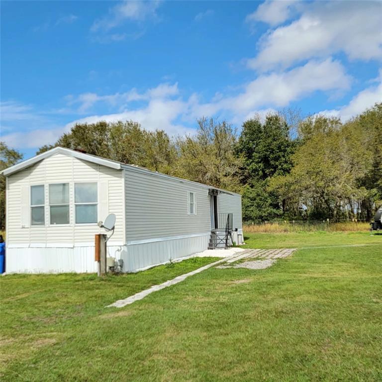 A light-colored mobile home sits on a grassy lot with a gravel patio area — 14626 MCGRADY ROAD, WIMAUMA, FL