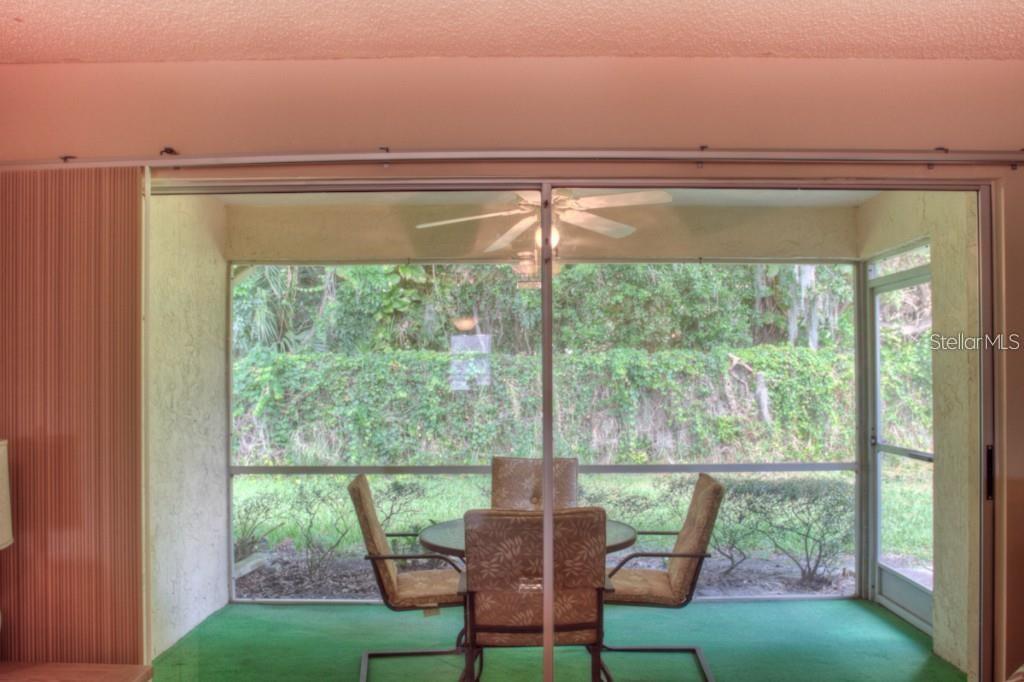 A screened-in patio features green carpeting, a dining set, and a view of dense foliage — 7062 W COUNTRY CLUB DRIVE N UNIT 7062, SARASOTA, FL