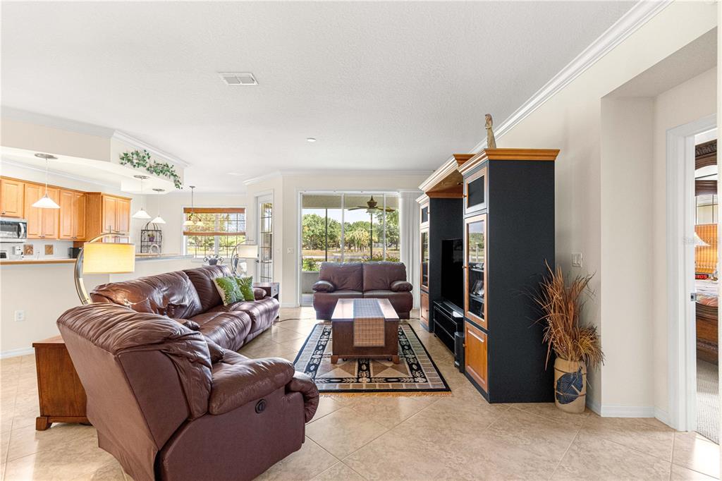 A living room with tile floors, a brown leather sofa, and a large entertainment center — 8355 SW 84TH LOOP, OCALA, FL