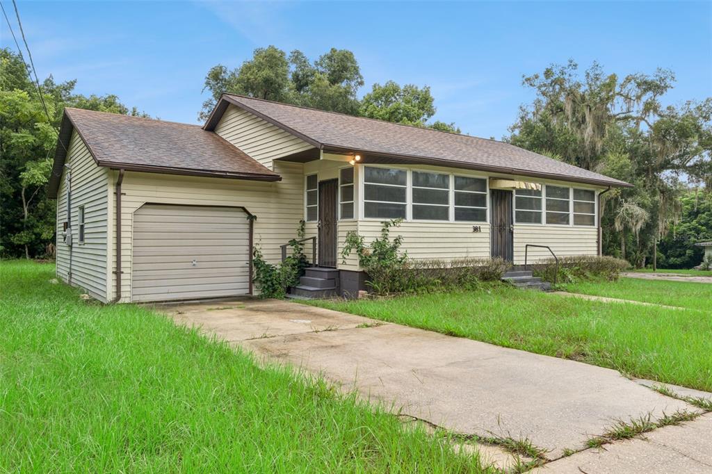 A single-story house with beige siding, a garage, and a concrete driveway sits on grass — 381 W OHIO AVENUE, LAKE HELEN, FL