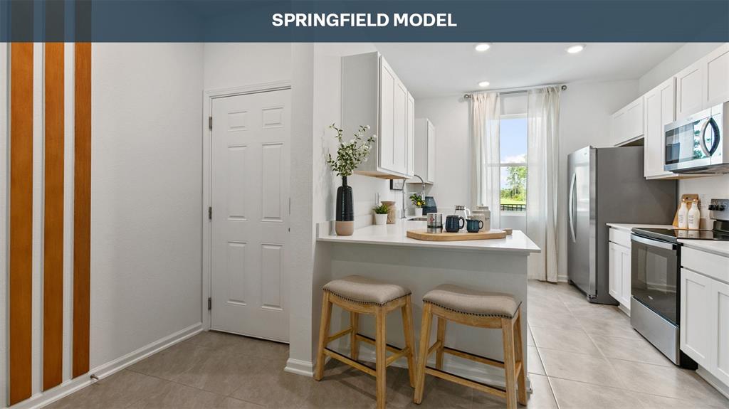 A kitchen features white cabinets, stainless steel appliances, a breakfast bar, and two wooden stools — 293 AYAMONTE ROAD, ST AUGUSTINE, FL