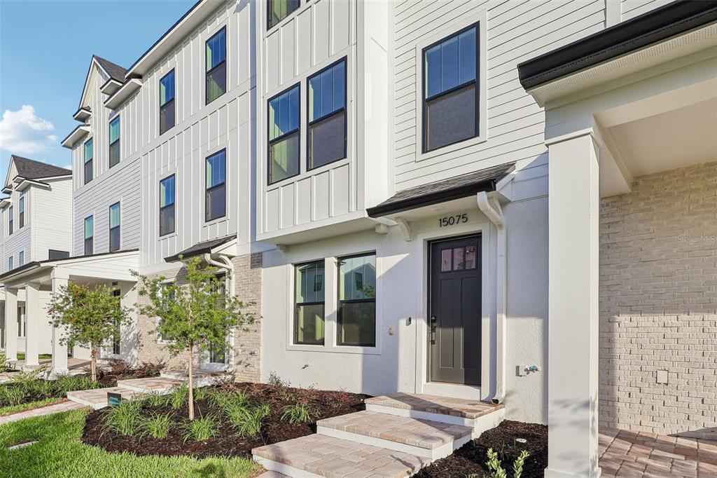 A three-story white townhouse exterior features black-framed windows and a light-colored front door — 15075 GROVESIDE ROAD, WINTER GARDEN, FL