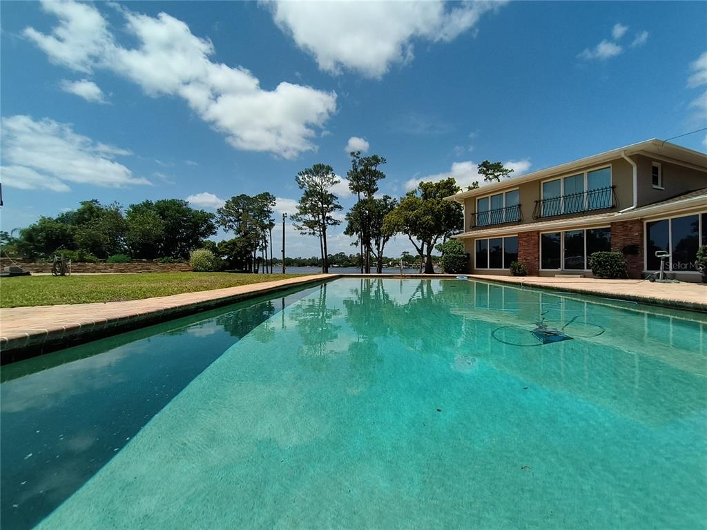 A large swimming pool sits in the backyard of a two-story house near a lake — 910 N KEPLER ROAD, DELAND, FL