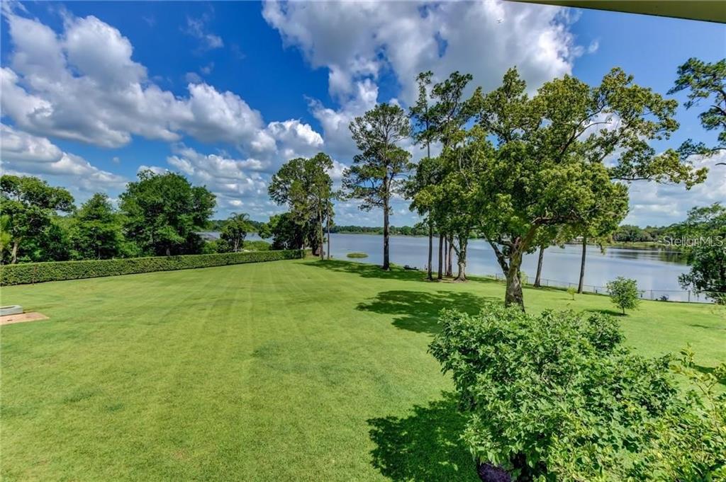 A large, manicured green lawn leads to a lake surrounded by mature trees — 910 N KEPLER ROAD, DELAND, FL