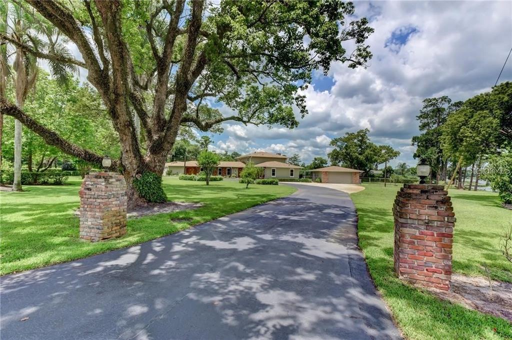 A paved driveway leads toward a house with a large tree and brick entrance pillars — 910 N KEPLER ROAD, DELAND, FL