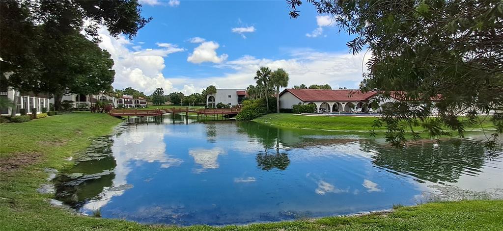 A pond with a wooden footbridge sits in front of apartment buildings and a pool — 7201 COUNTRY CLUB DRIVE UNIT G21, LAKE WALES, FL
