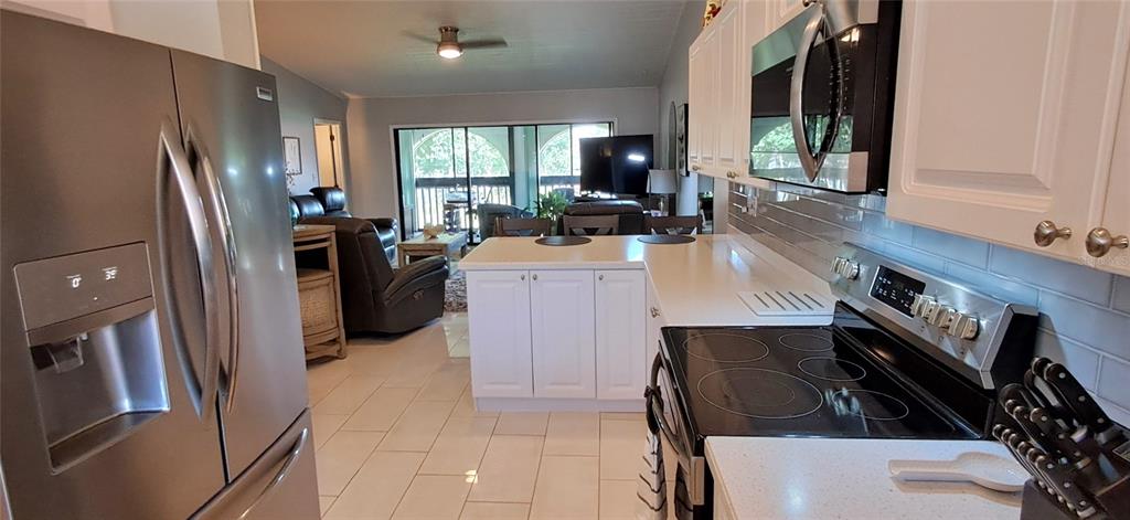 A kitchen with white cabinets and stainless steel appliances opens into a living room area — 7201 COUNTRY CLUB DRIVE UNIT G21, LAKE WALES, FL