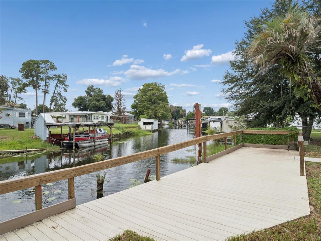 A wooden deck overlooks a narrow canal lined with boat docks and residential structures — 13602 PALM DRIVE, ASTATULA, FL