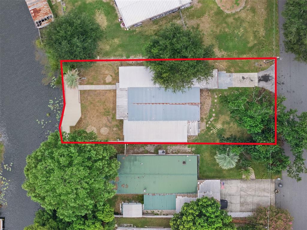 An aerial view shows a house with a metal roof situated on a waterfront lot — 13602 PALM DRIVE, ASTATULA, FL