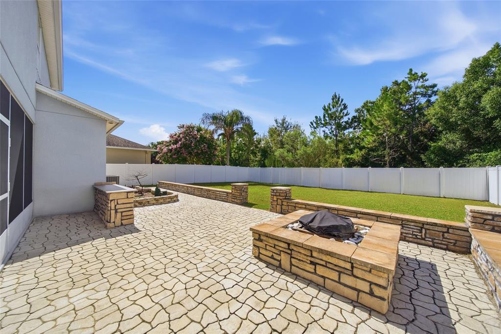A backyard patio features a stone fire pit, low retaining walls, and a white privacy fence — 12125 STREAMBED DRIVE, RIVERVIEW, FL