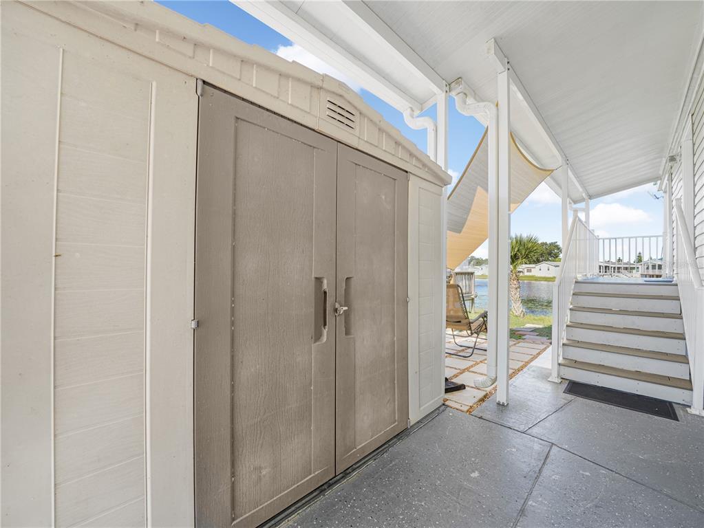 A beige storage shed sits on a concrete patio next to stairs leading to a deck — 16 QUEEN OF WATERS STREET, LAKE WALES, FL