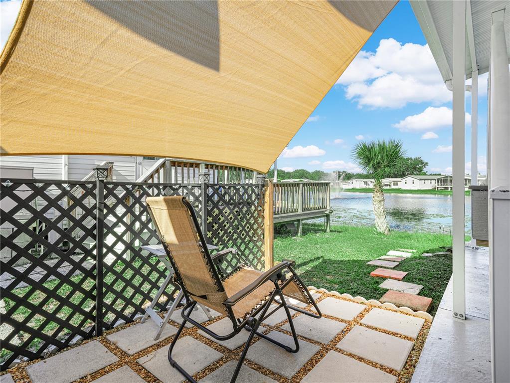 A patio with a lounge chair, lattice privacy screen, and shade sail overlooks a pond — 16 QUEEN OF WATERS STREET, LAKE WALES, FL